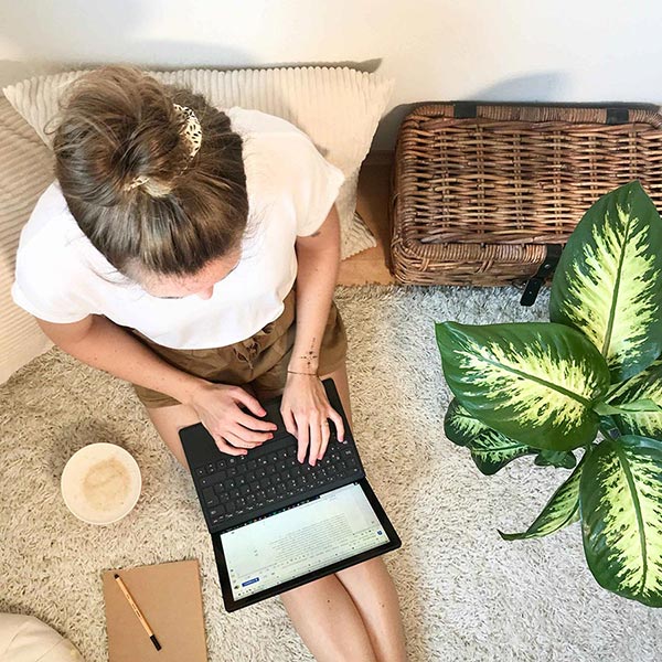 Frau sitzt mit einem Laptop auf dem Boden und schreibt in ein Dokument.
